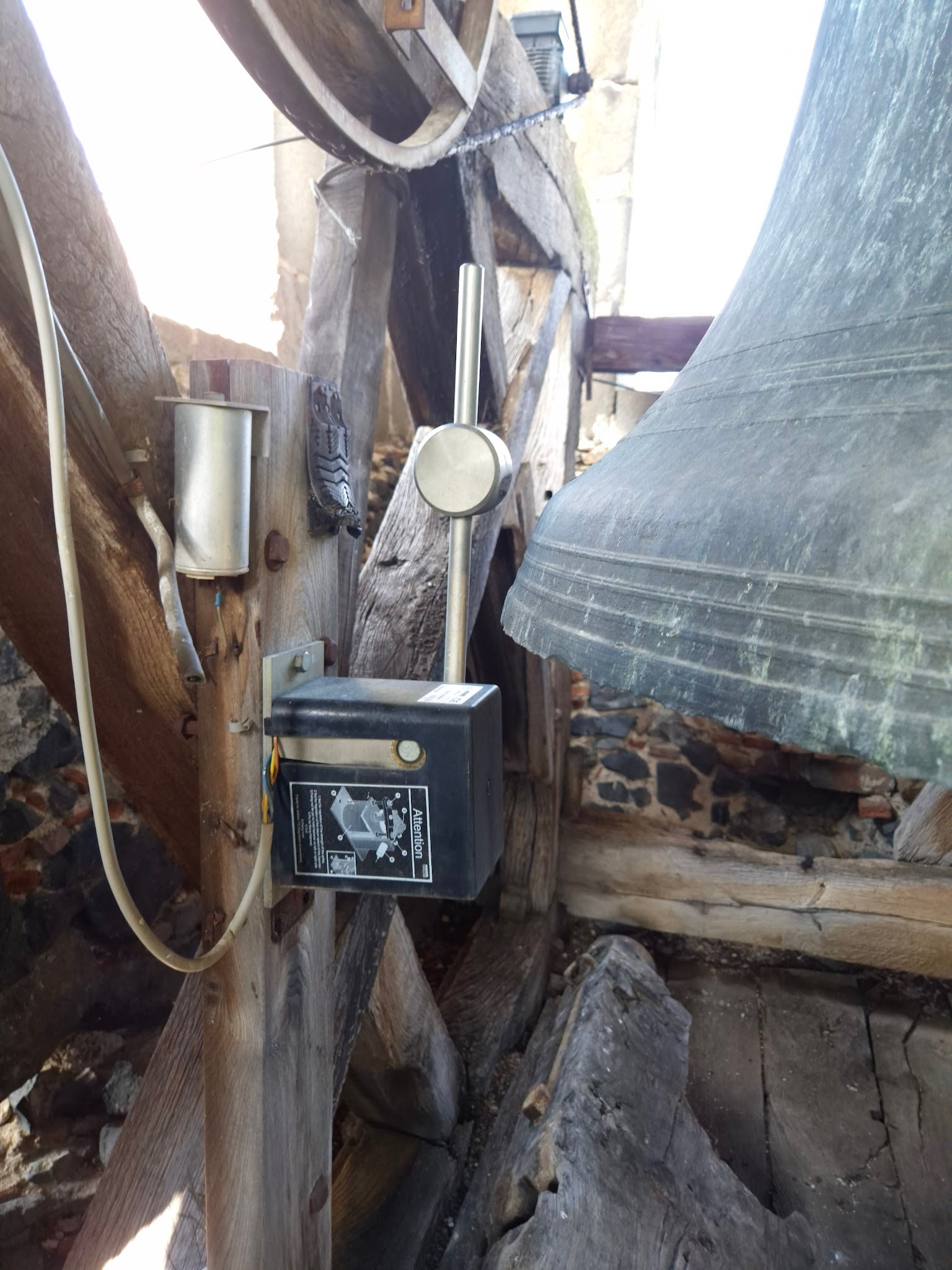 Marteau de tintement électrique et son boîtier fixés au beffroi, à côté d’une cloche d’église