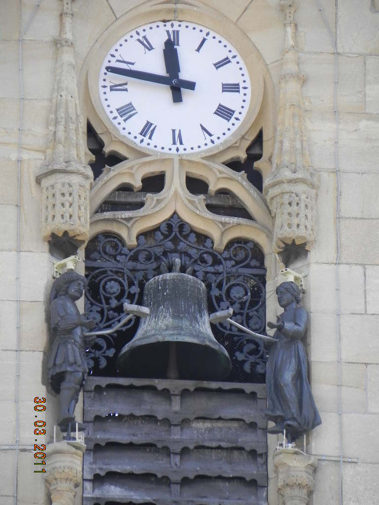 Cadran d’horloge à chiffres romains au-dessus d’une cloche de façade encadrée de deux automates